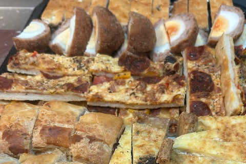 A platter of food consisting of quiche, pizza and scotch eggs.